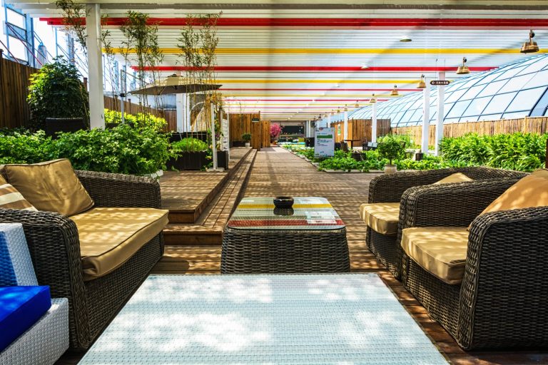 Salon de jardin couvert avec fauteuils en osier et plantes vertes.